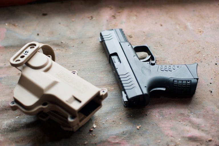 A Black Pistol Beside a Beige Gun Case on a Dirty Surface