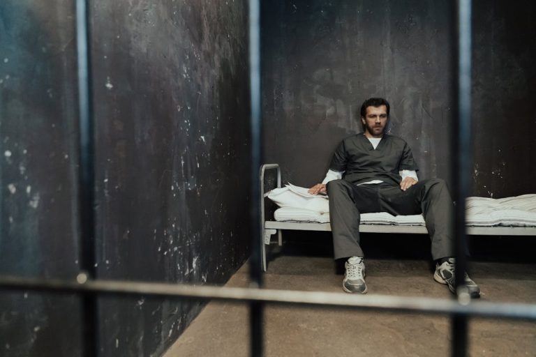 Man Sitting on Bed in Prison Cell
