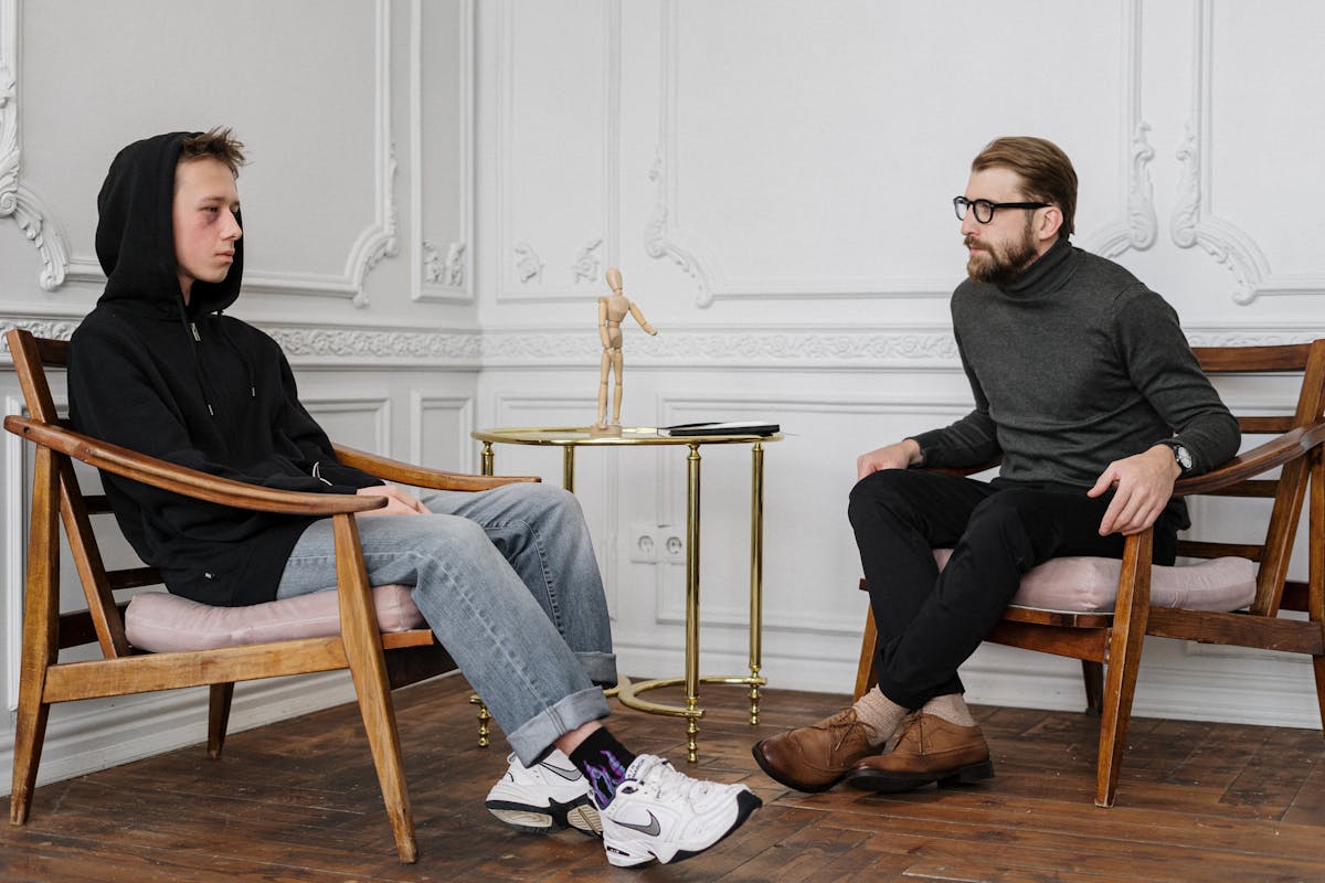 Man in Black Sweater and Blue Denim Jeans Sitting on Brown Wooden Chair