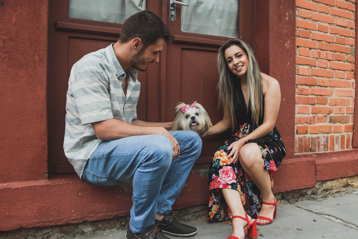 Photo of Smiling Couple Petting a Shih Tzu While Sitting