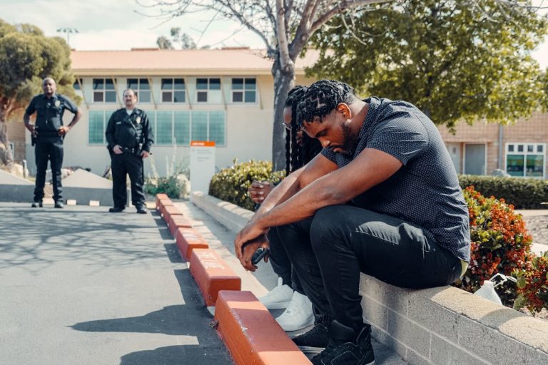 Police officers observing two adults sitting on a curb